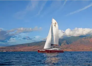 Red sailboat with white sails sailing on ocean with cloud-covered mountains in background