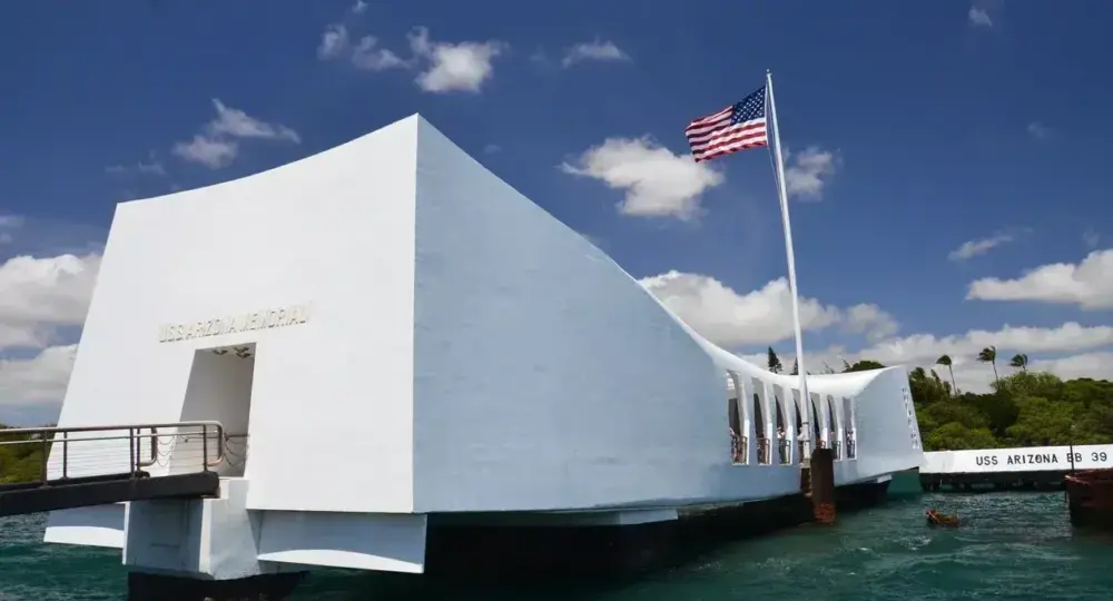 USS Arizona Memorial white structure over water with American flag under blue sky