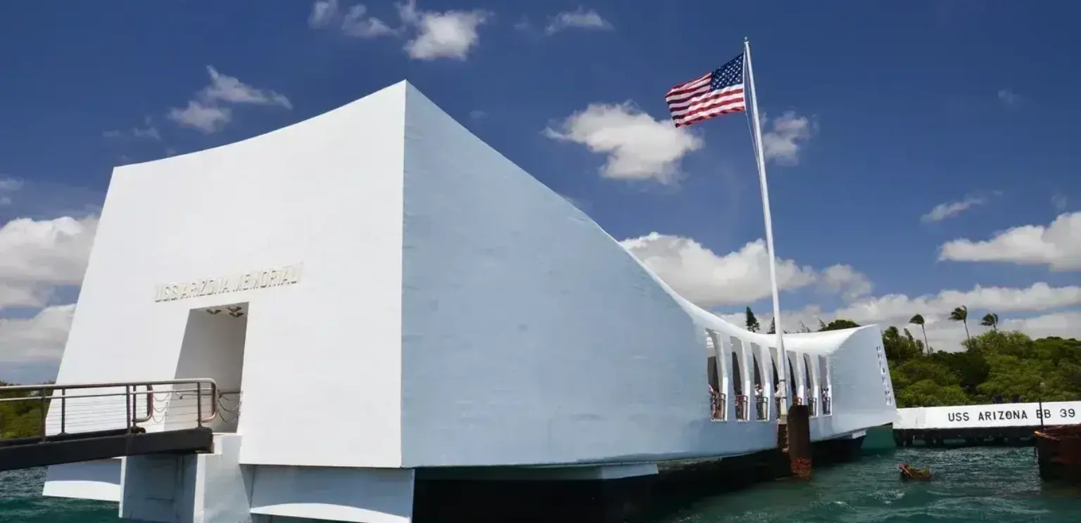 USS Arizona Memorial white structure over water with American flag under blue sky