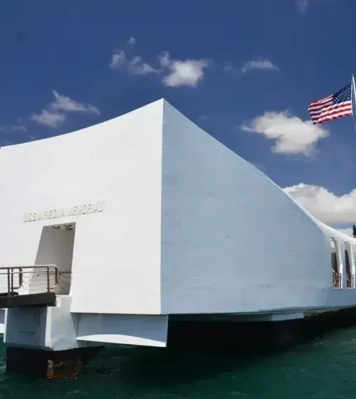 USS Arizona Memorial white structure over water with American flag under blue sky