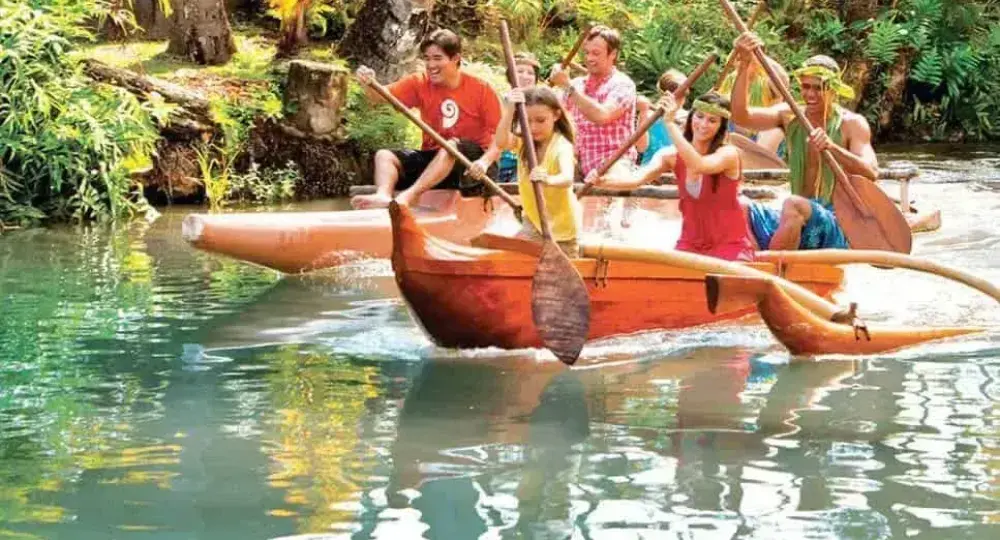 group of people paddling an outrigger canoe on a tropical river surrounded by green foliage