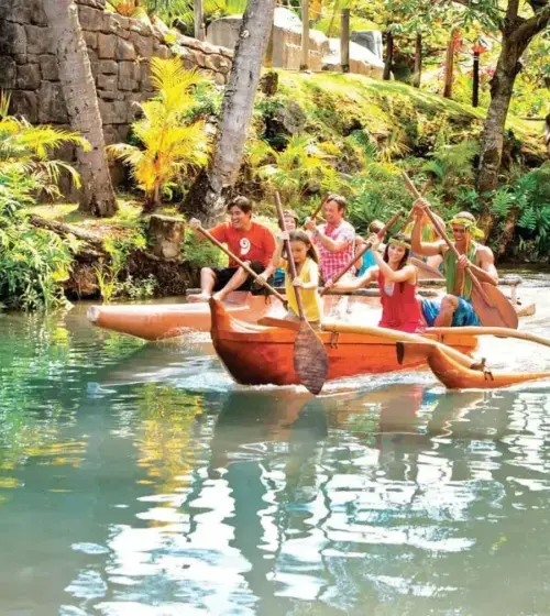 group of people paddling an outrigger canoe on a tropical river surrounded by green foliage