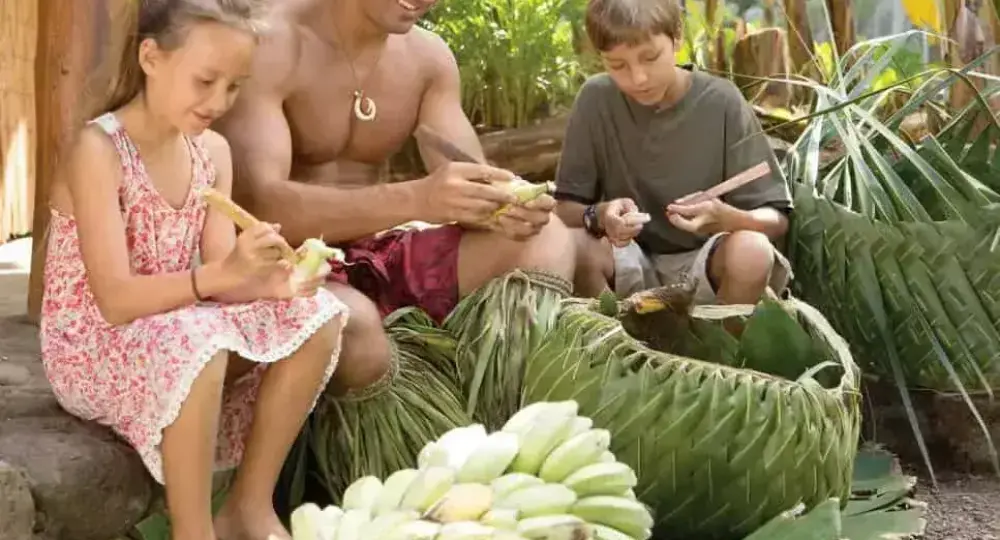 Hawaiian man teaching two children to peel bananas in tropical setting