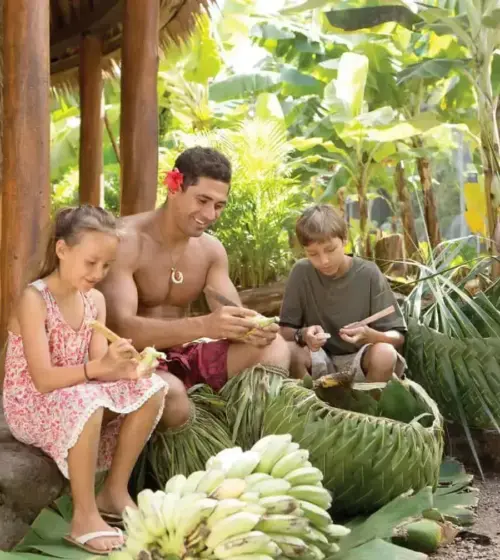 Hawaiian man teaching two children to peel bananas in tropical setting