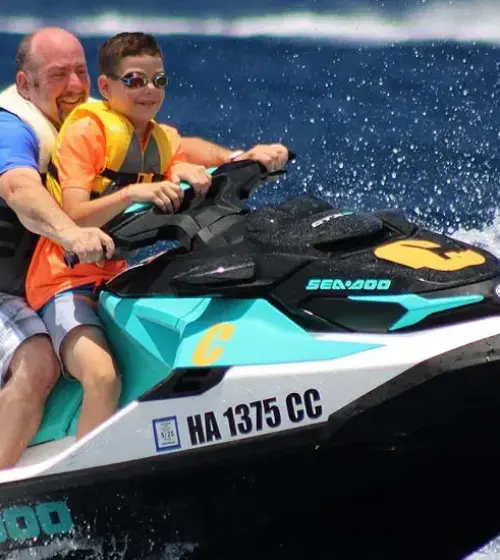 family of three wearing life jackets riding a sea-doo jet ski on blue ocean water