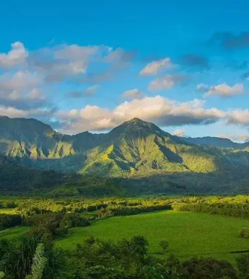 Mountain range with green fields under blue sky and scattered clouds
