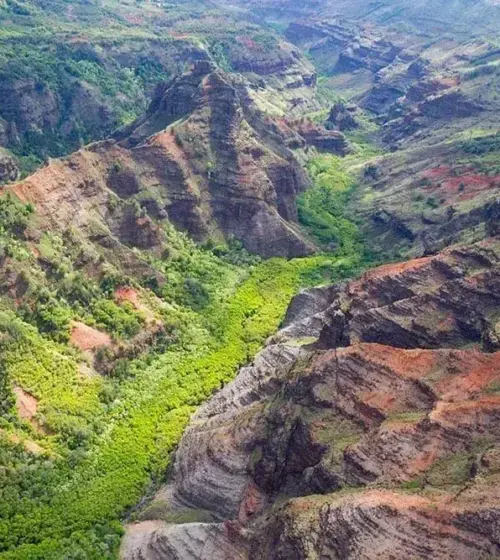 Aerial view of a Hawaiian canyon with rugged rocky ridges and vibrant green river valley