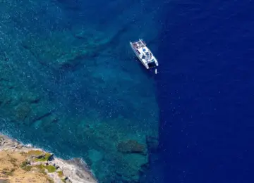 white boat floating on clear blue ocean water near rocky coastline