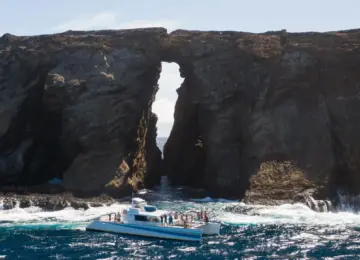 Catamaran with people near rocky sea arch in blue ocean