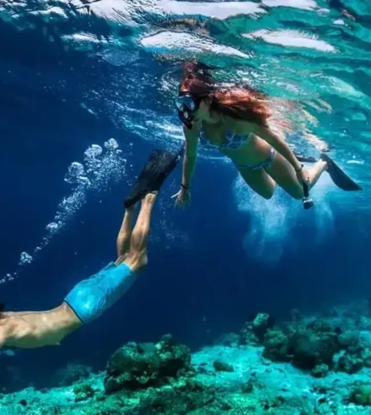 Two snorkelers swimming underwater over coral reef in clear blue ocean