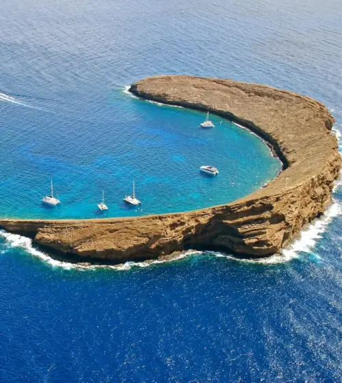 Molokini Crater surrounded by deep blue ocean with boats anchored inside clear blue waters