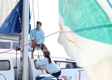 two people operating sails on a catamaran near rocky coastline
