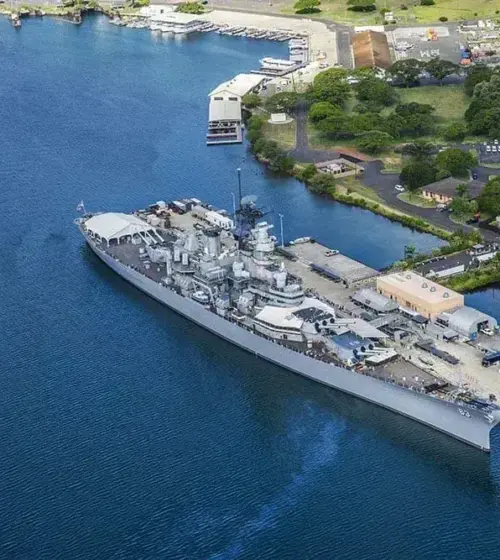 naval battleship docked at harbor with surrounding water and nearby buildings