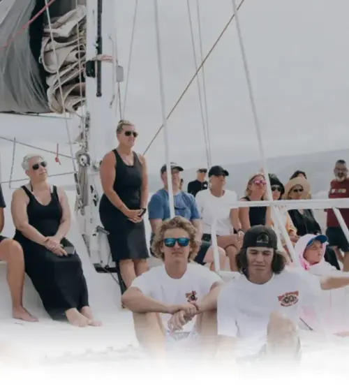 diverse group of people sitting and standing on a sailboat under cloudy sky