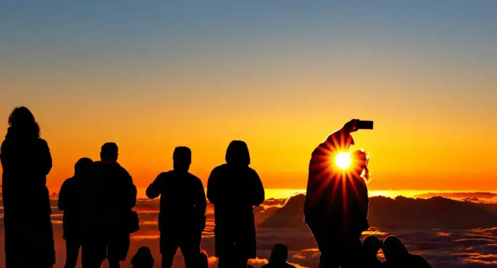 Group of people silhouetted against a sunset with sun flare over clouds