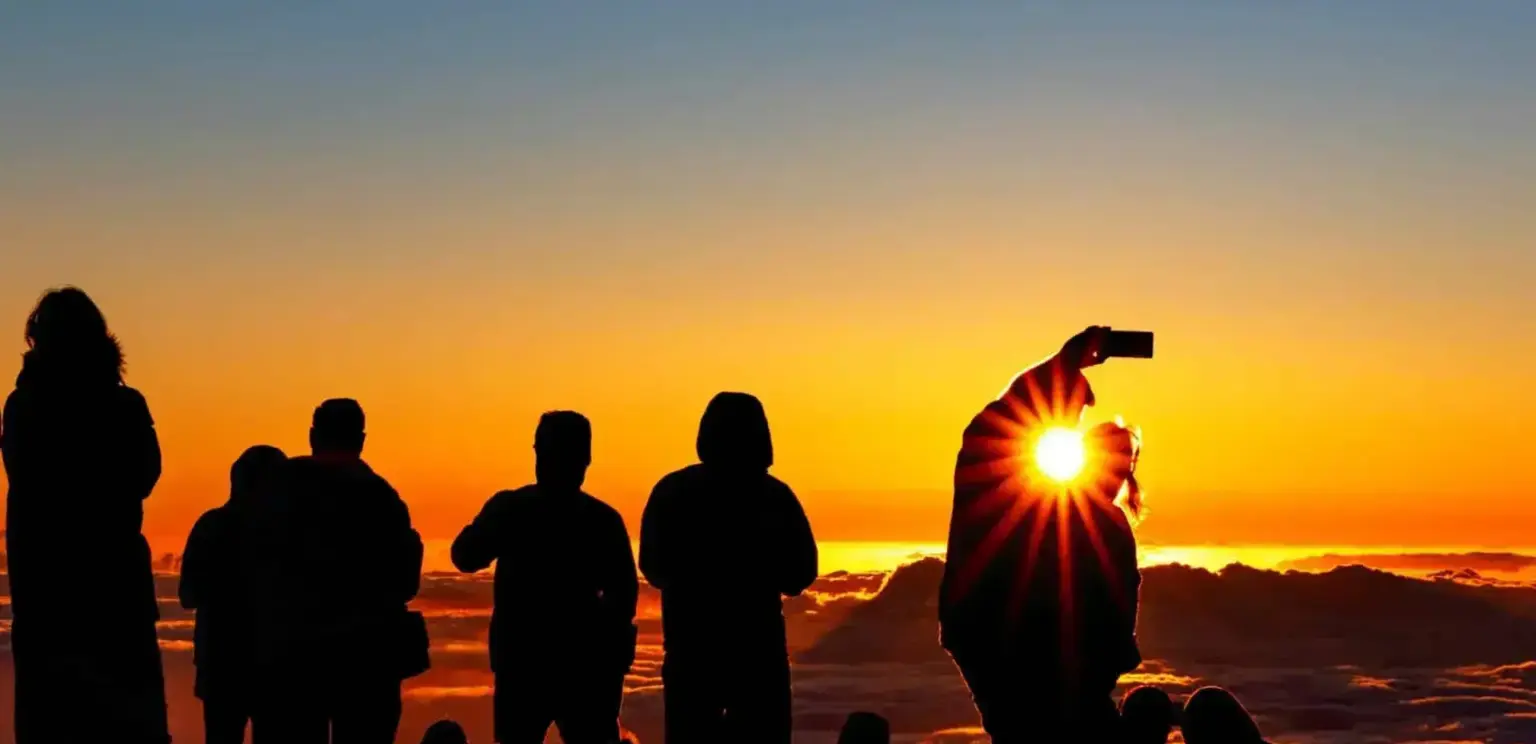 Group of people silhouetted against a sunset with sun flare over clouds
