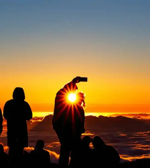 Group of people silhouetted against a sunset with sun flare over clouds
